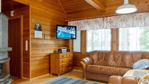 A cozy cabin interior with a wooden interior, a leather sofa, a television, and a fireplace.