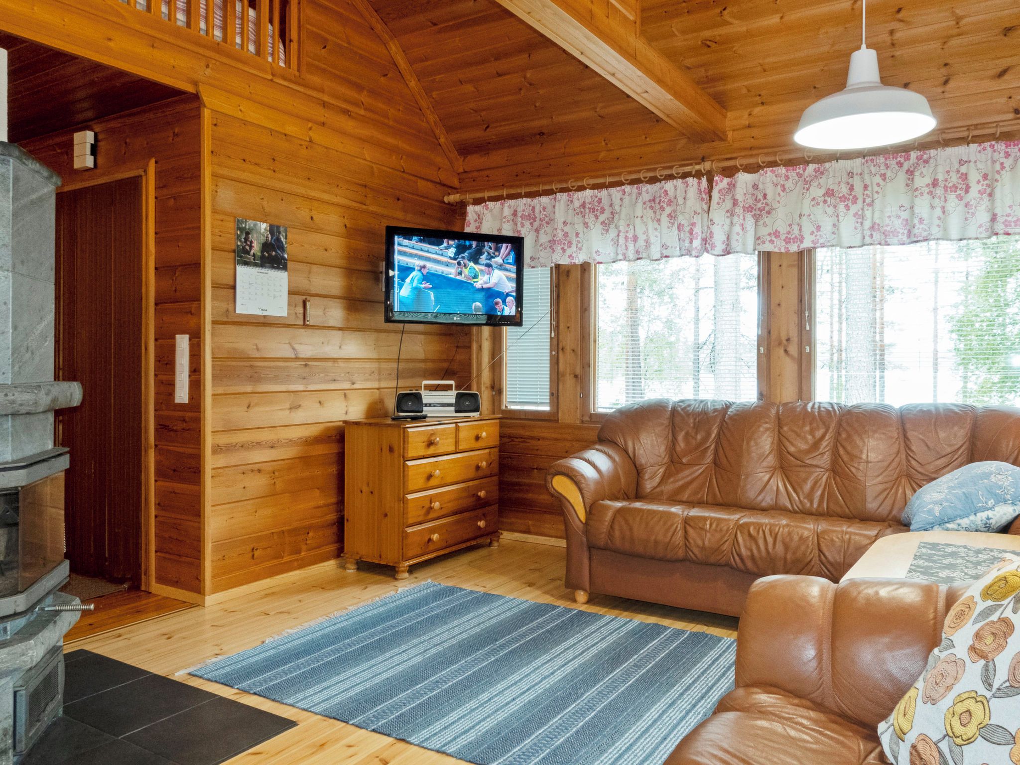 Un salon chaleureux avec un décor intérieur en bois, un téléviseur fixé au mur, un canapé en cuir et une cheminée.