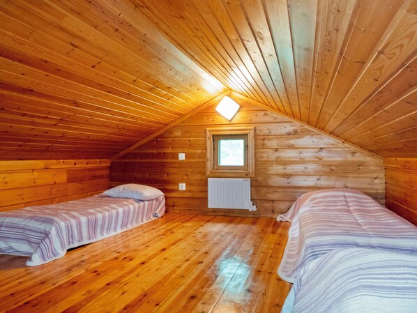 A cozy attic bedroom with wooden walls and sloped ceilings, featuring two single beds with striped bedding.