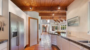 Een moderne keuken met een centraal eiland, roestvrijstalen apparatuur en een houten plafond.