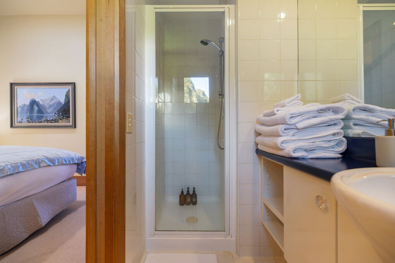 A bathroom with a glass-enclosed shower, a sink, and a stack of towels.