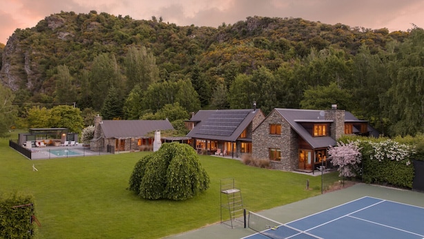 Een groot huis met een tennisbaan, een zwembad en een verzorgd gazon.