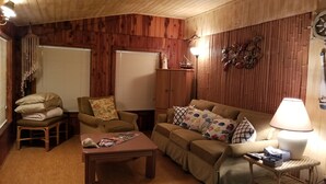 A cozy living room with wooden paneling, a sofa, a chair, a coffee table, and a lamp.