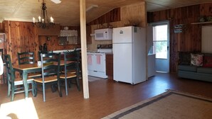 A kitchen with wooden walls, a dining table with chairs, a white refrigerator, a microwave, and a stove.