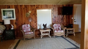 A cozy room with wooden walls, two wicker chairs with patterned cushions, a small table, a decorative fan, and a television mounted on the wall.