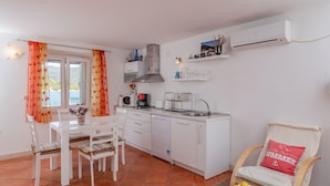 Una cucina compatta con mobili bianchi, una macchina da caffè e un lavandino. C'è un tavolo da pranzo con sedie e una sedia con cuscino.
