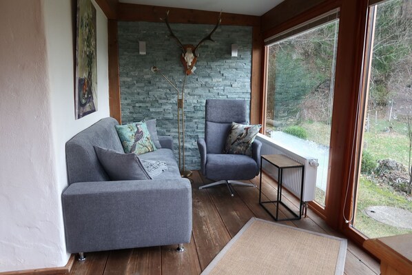 Una habitación acogedora con un sofá y un sillón grises, una pared de piedra y vistas al exterior.