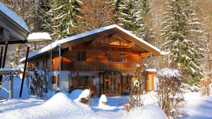 Une cabane en bois dotée d’un grand porche et d’une entrée couverte, entourée d’arbres recouverts de neige.