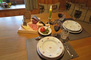 A dining table set with plates, cutlery, a candle, and a cheese board with various meats and pickles.