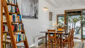 A dining area with a wooden table, chairs, a bookshelf, and a view of the outdoors.