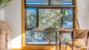 A room with a large window overlooking a body of water and trees. There is a wooden chair and a table near the window.