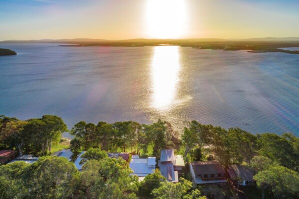 A coastal landscape with a body of water reflecting sunlight, surrounded by greenery and residential buildings. - Villa Belza - Lakeside cottage near Angourie beaches (Wooloweyah)