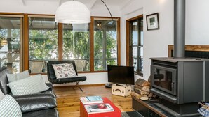 A modern living room with a leather sofa, a red coffee table, a television, and a wood-burning stove.