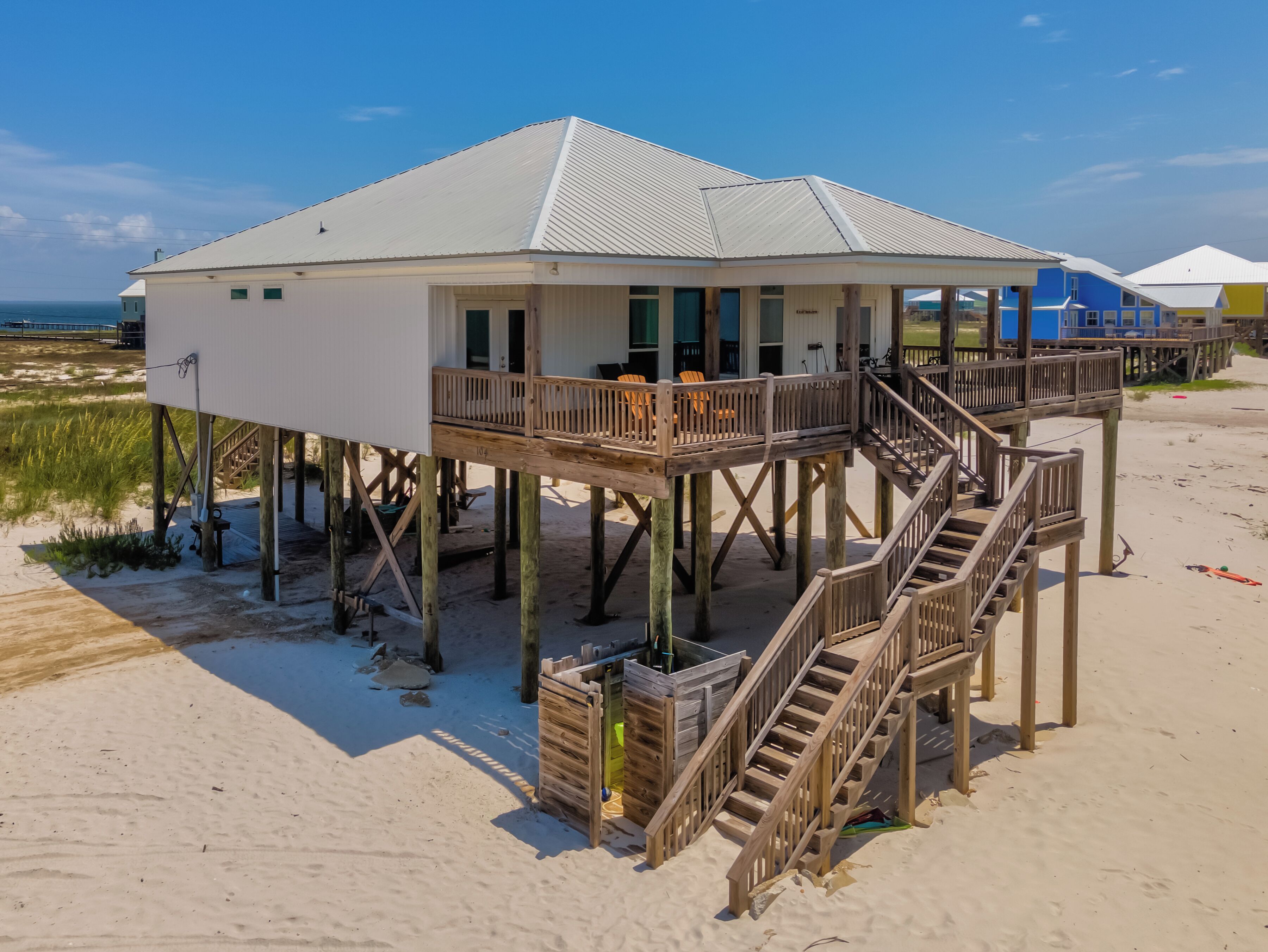 A beach house with a wooden deck and stairs leading to a balcony.