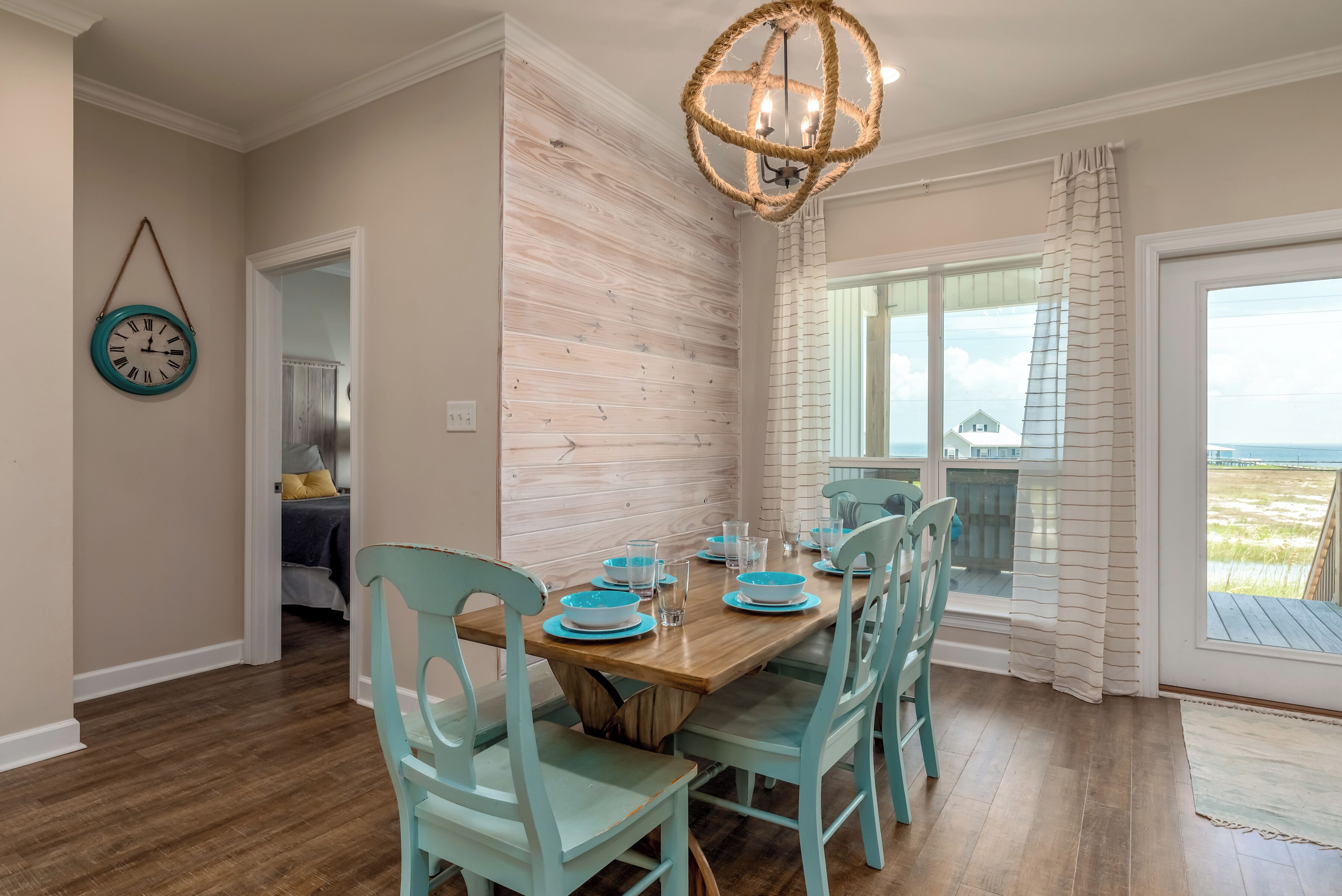 A dining area with a wooden table set for four, teal chairs, and a hanging light fixture.