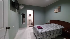 Quarto com cama, mesa de cabeceira, televisão na parede e porta para um banheiro.