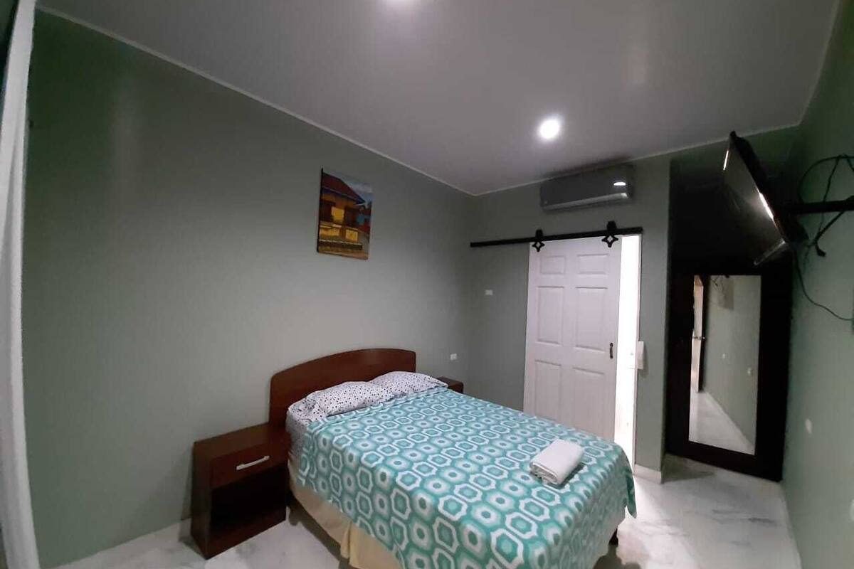A bedroom with a bed, a nightstand, a door, and a mirror.