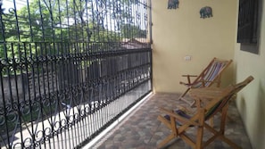 Un balcón con reja de hierro forjado, una silla de madera y una mesita.