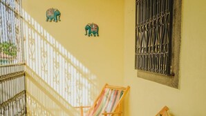 Uma varanda com duas cadeiras de madeira, piso de azulejos e arte decorativa de elefantes na parede.