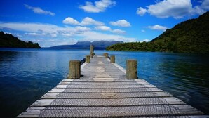 A wooden pier extending into calm water, surrounded by lush greenery and mountains in the distance.
