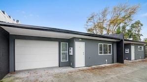 A modern two-story building with a grey exterior, a white garage door, and a small attached structure.