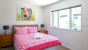 A bedroom with a bed, two bedside tables, a window, and a painting on the wall.