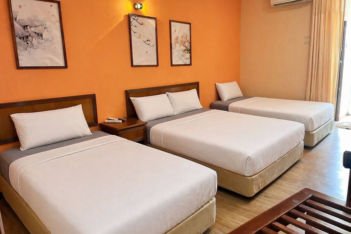 A hotel room with three beds, a wooden floor, and a wall-mounted air conditioner.