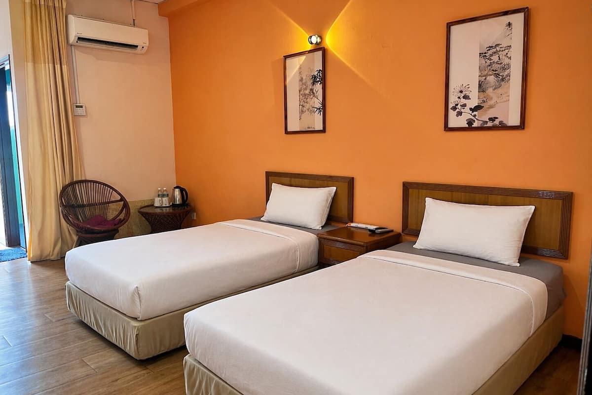 A hotel room with two beds, a chair, a nightstand, and two wall-mounted artworks.