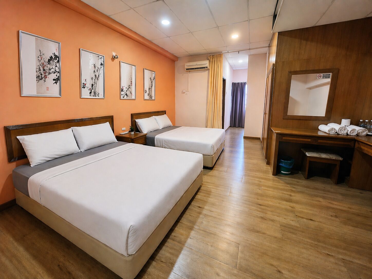 A hotel room with two beds, a desk, a chair, a mirror, and artwork on the wall.
