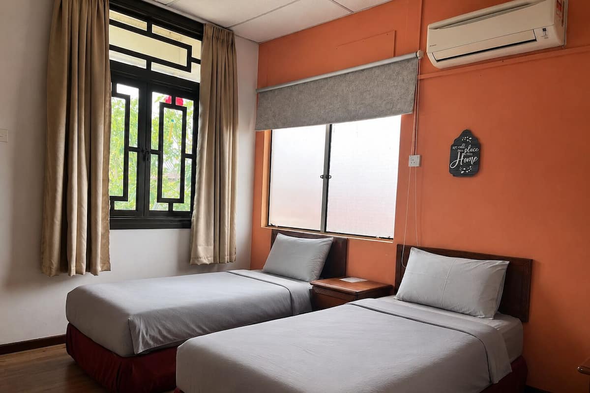 A room with two beds, a window with curtains, an air conditioning unit, and a wall-mounted sign.
