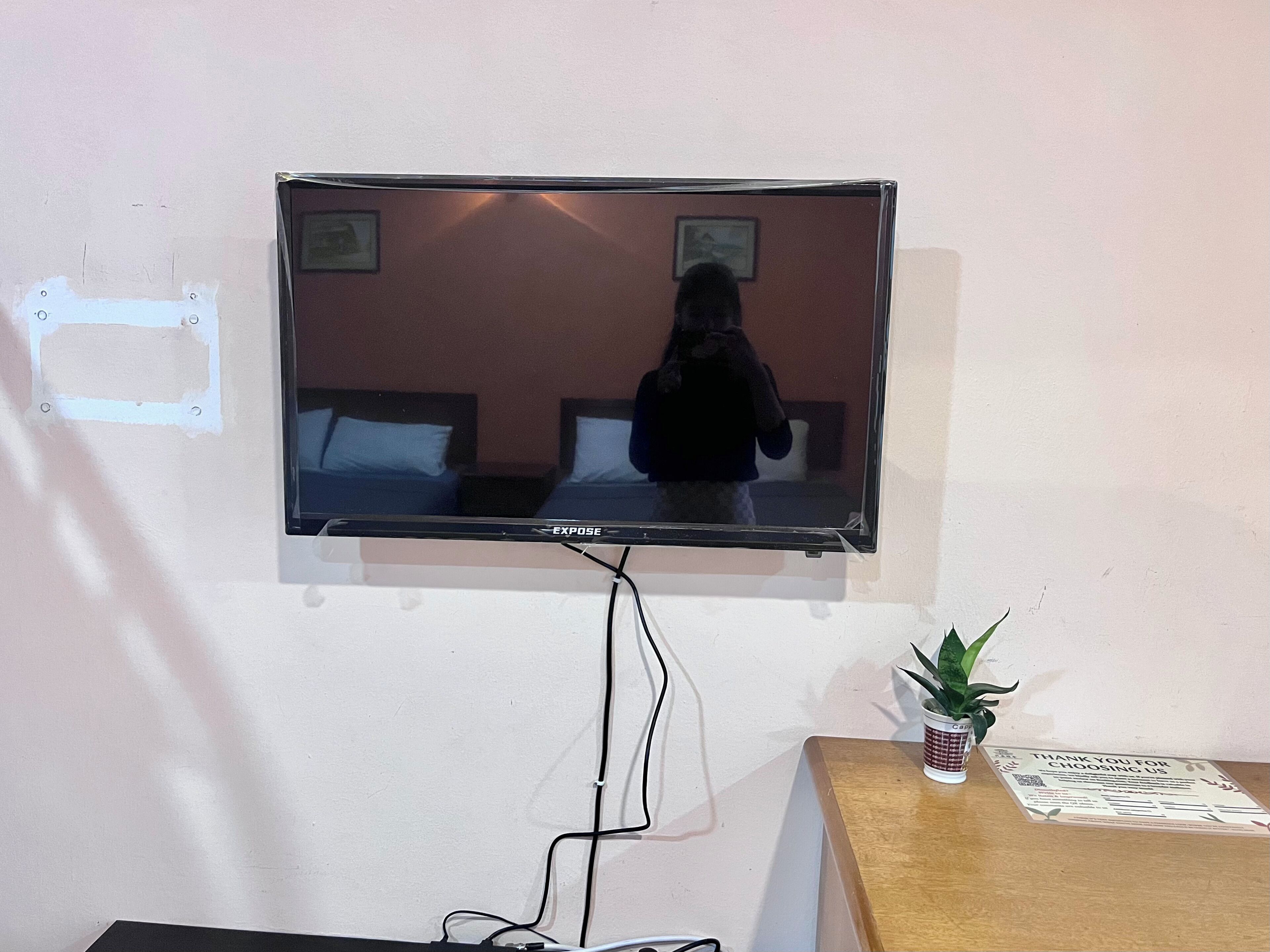 Un televisor montado en la pared, con una cama y una mesita de noche debajo.