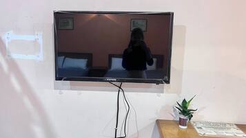 Un televisor montado en la pared, con una cama y una mesita de noche debajo.