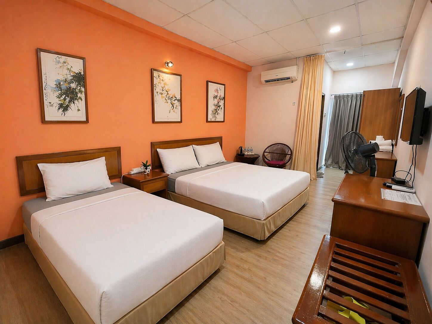 Een hotelkamer met twee bedden, een bureau, een stoel, een airconditioning en kunstwerken aan de muren.