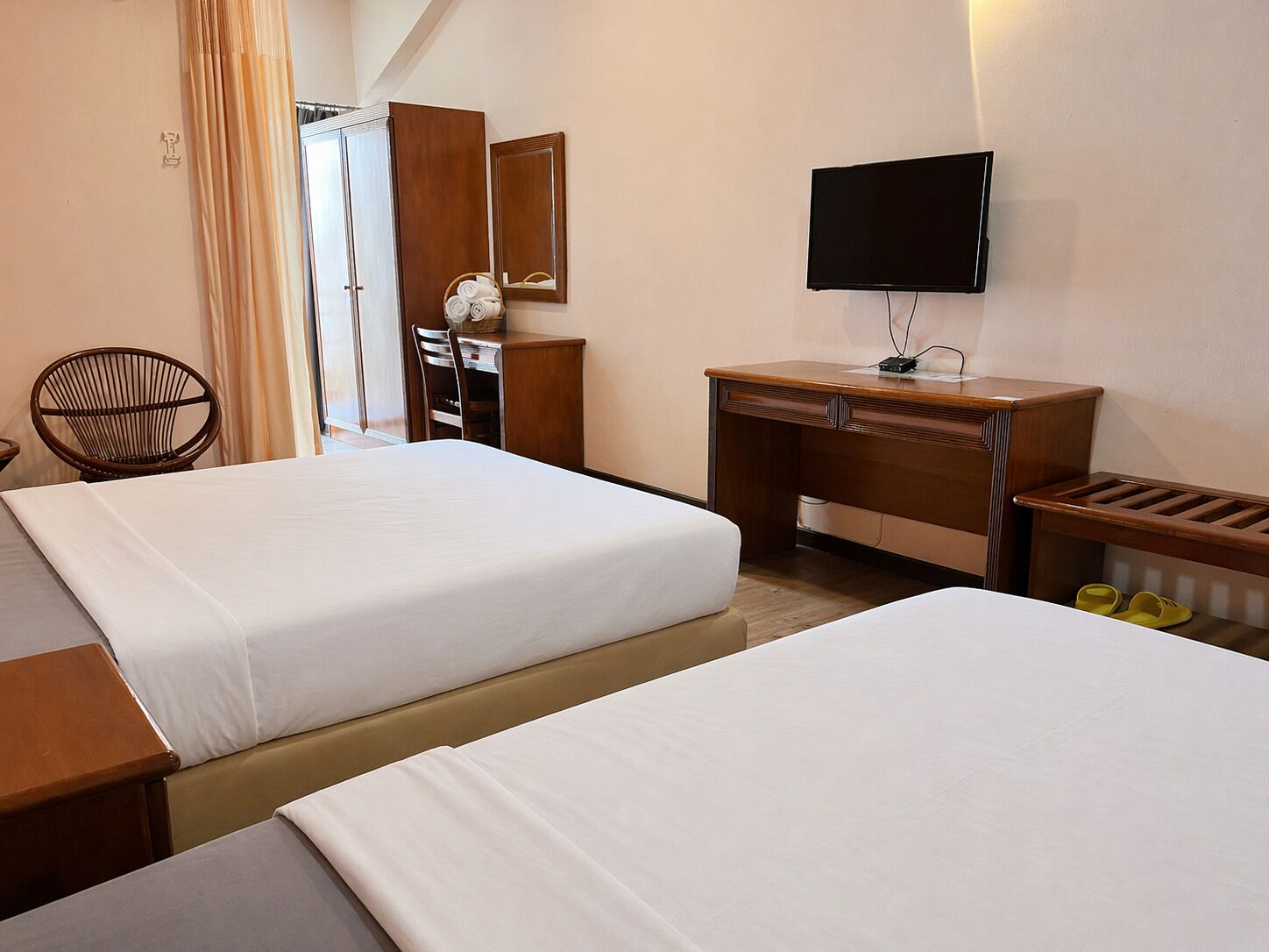 A hotel room with two beds, a desk, a chair, a television, and a mirror.