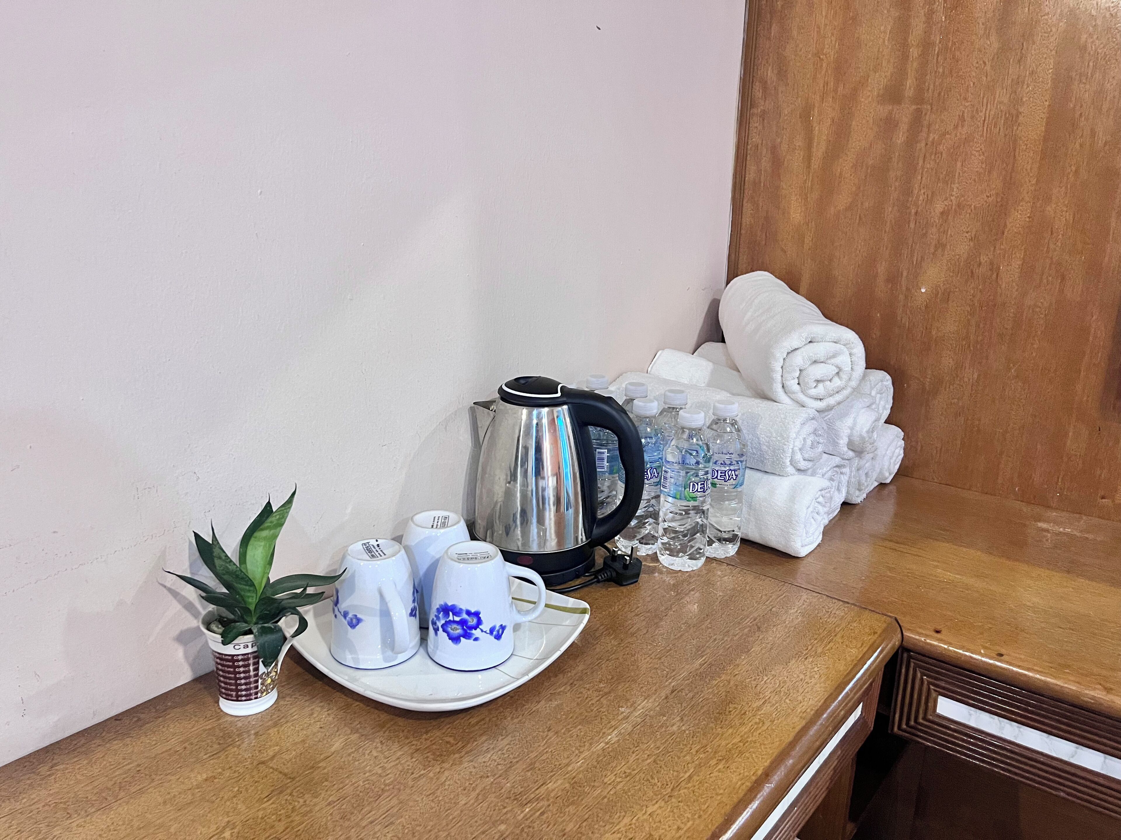 Una mesa ordenada con cafetera, botellas de agua, toallas y una planta en maceta.