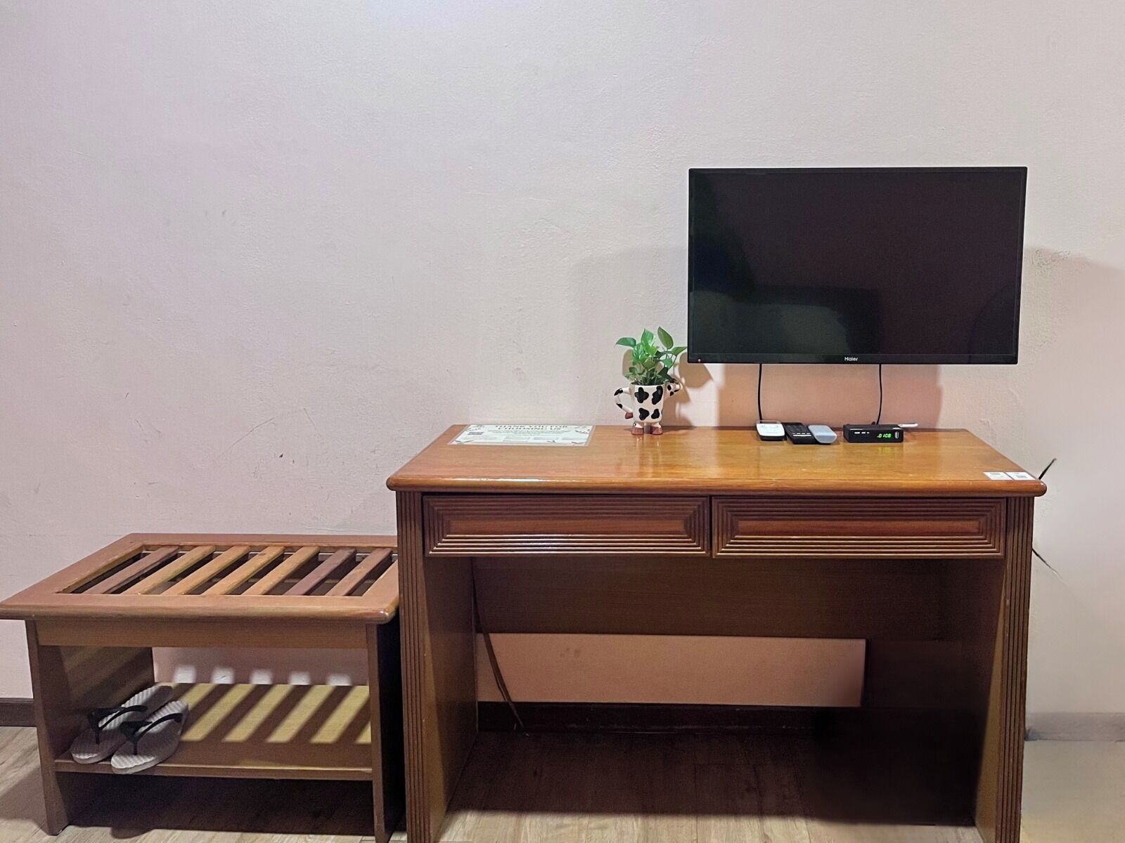 Un escritorio de madera con un televisor de pantalla plana, una planta pequeña y un control remoto.