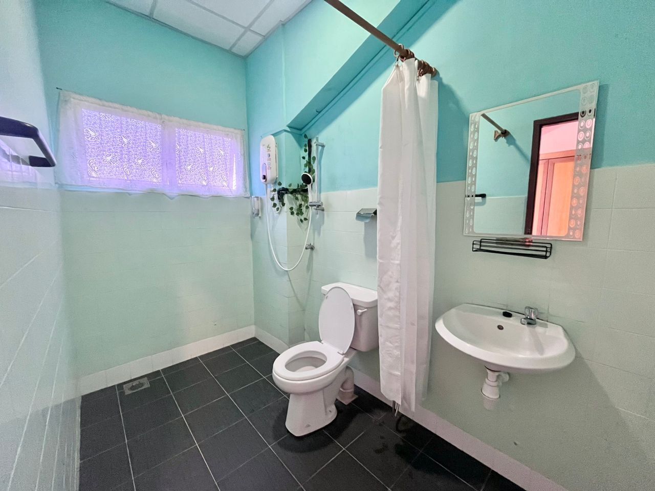 Une salle de bain comprenant des toilettes, un lavabo, une douche avec un rideau et une fenêtre décorée de papier.