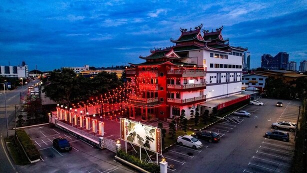 Un edificio de varios pisos con arquitectura tradicional, que destaca por una entrada iluminada en rojo y un estacionamiento frente a él.
