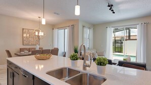 Een moderne keuken met een dubbele spoelbak, roestvrijstalen apparatuur en een eethoek met een tafel en stoelen.