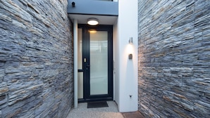 A modern building entrance with a stone facade, a glass door, and a small overhang above the door. - 3-BDR Apartment with Panoramic Views & Fireplace (Queenstown)