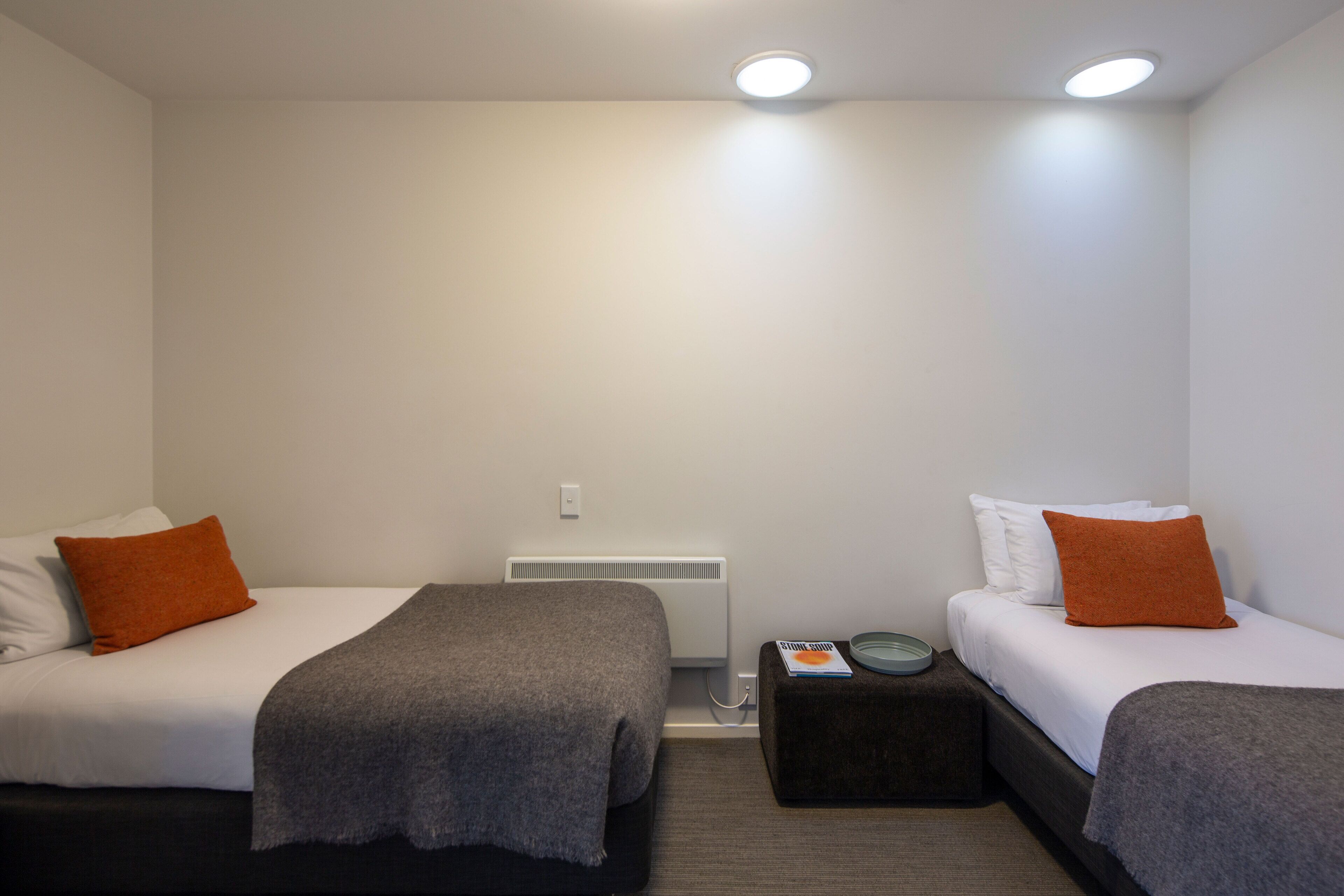 A hotel room with two beds, each with a pillow and a blanket.