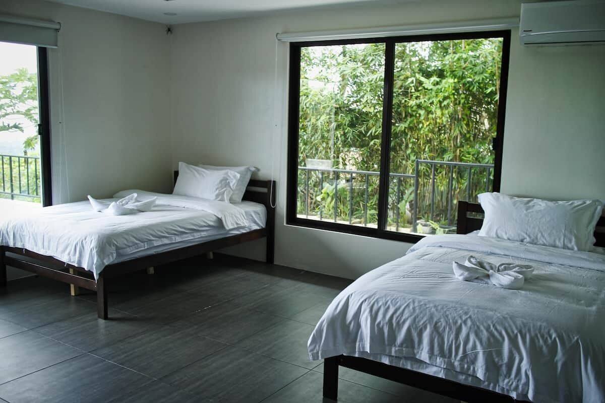 A hotel room with two beds, large windows with a view of greenery, and a balcony.