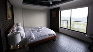 A bedroom with a large window, a ceiling fan, a bed with white linens, and a bedside table with a lamp and a small plant. - Bituin sa Tala (Orani)
