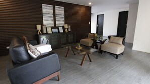 A modern living room with a black leather sofa, a beige armchair, a glass coffee table, and a dark wooden accent wall with framed artwork. - Bituin sa Tala (Orani)