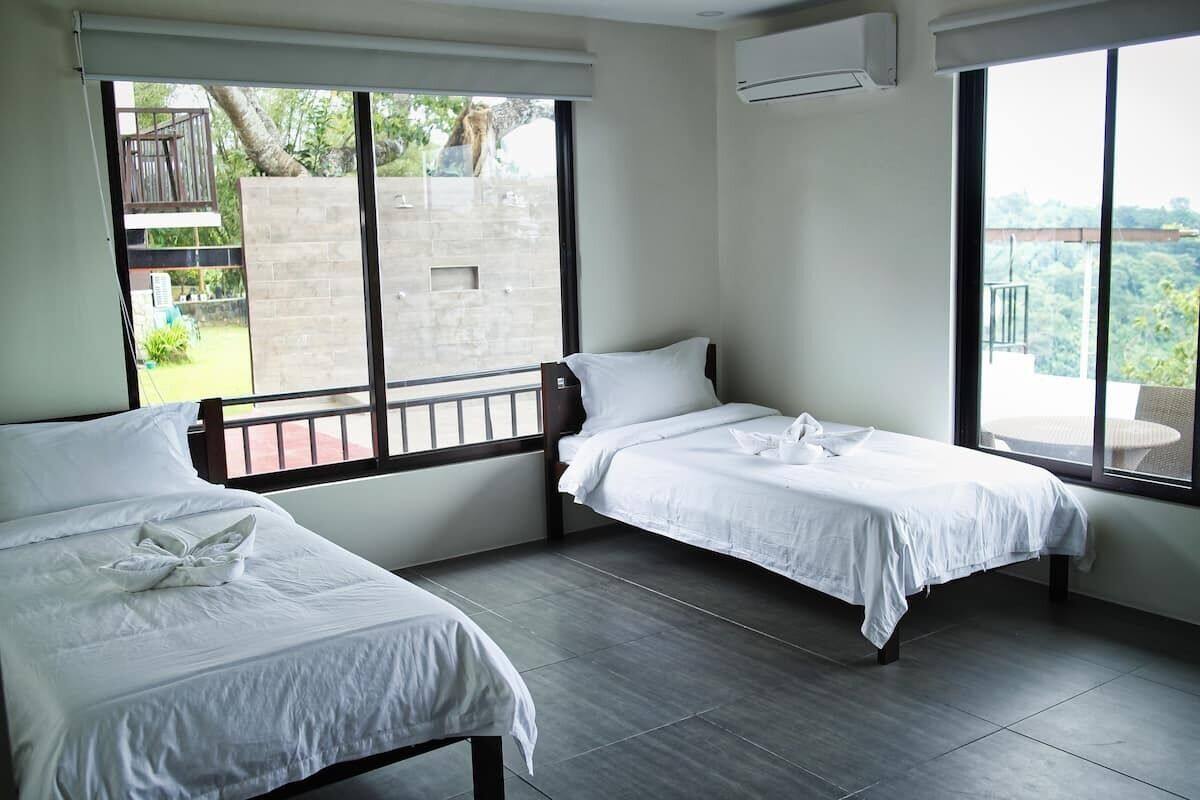 A hotel room with two single beds, large windows, and a balcony.