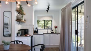 A modern kitchen with white cabinets, a built-in oven, and a window with a view of trees. - Acacia @ Bodhi - Cottage 2, a tranquil retreat 5 mins from Daylesford (Daylesford)