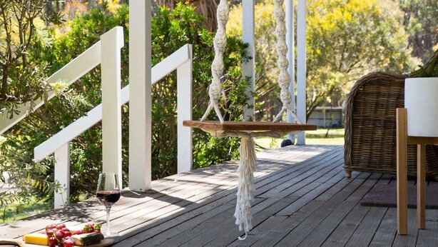 A wooden deck with a white railing, a table with a rope backrest, a glass of red wine, and a basket of grapes and strawberries. - Acacia @ Bodhi - Cottage 2, a tranquil retreat 5 mins from Daylesford (Daylesford)