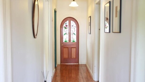 A hallway with a wooden floor, a wooden door with a stained glass window, and framed pictures on the walls.