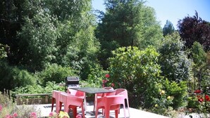 An outdoor patio with a table and chairs, surrounded by lush greenery and flowering plants.