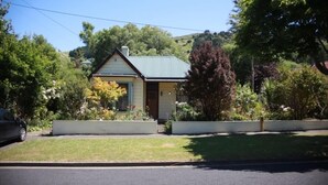A small, single-story house with a gabled roof, surrounded by lush greenery and a well-maintained lawn.